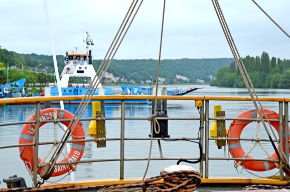 Blick auf ein Boot im Hafen mit Rettungsringen und ruhigem Wasser im Hintergrund.